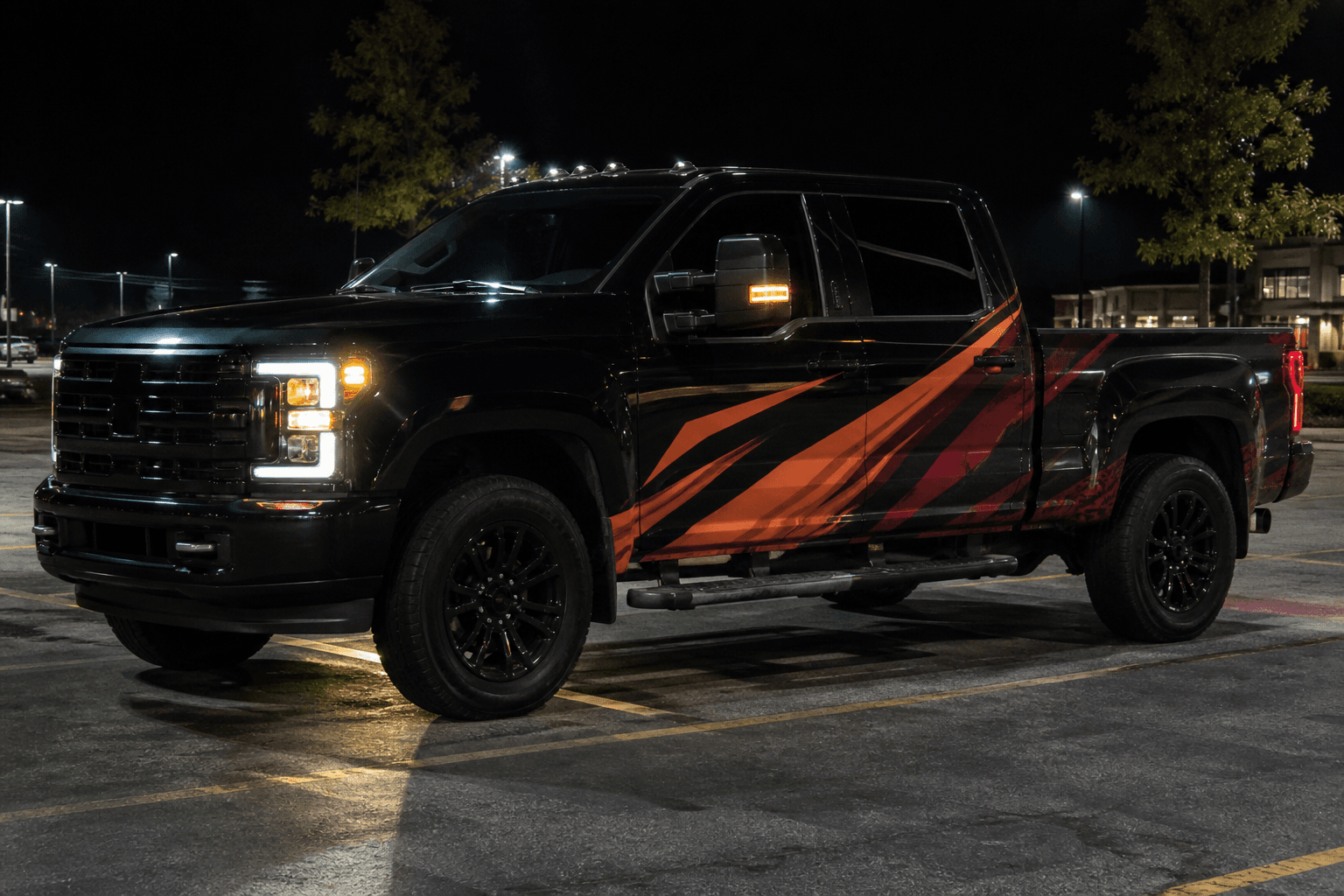 Black work truck with orange and crimson wrap graphics at night